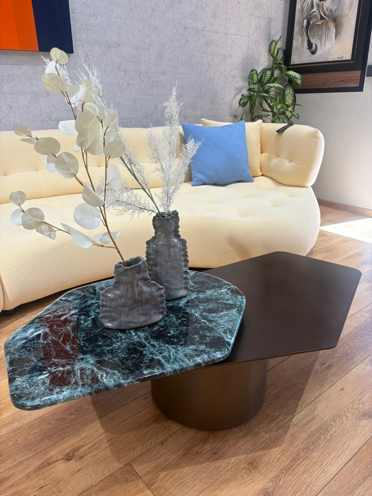 Table basse design contemporaine avec plateau asymétrique noir mat et effet marbre vert foncé, posée sur un pied cylindrique central dans un salon moderne.