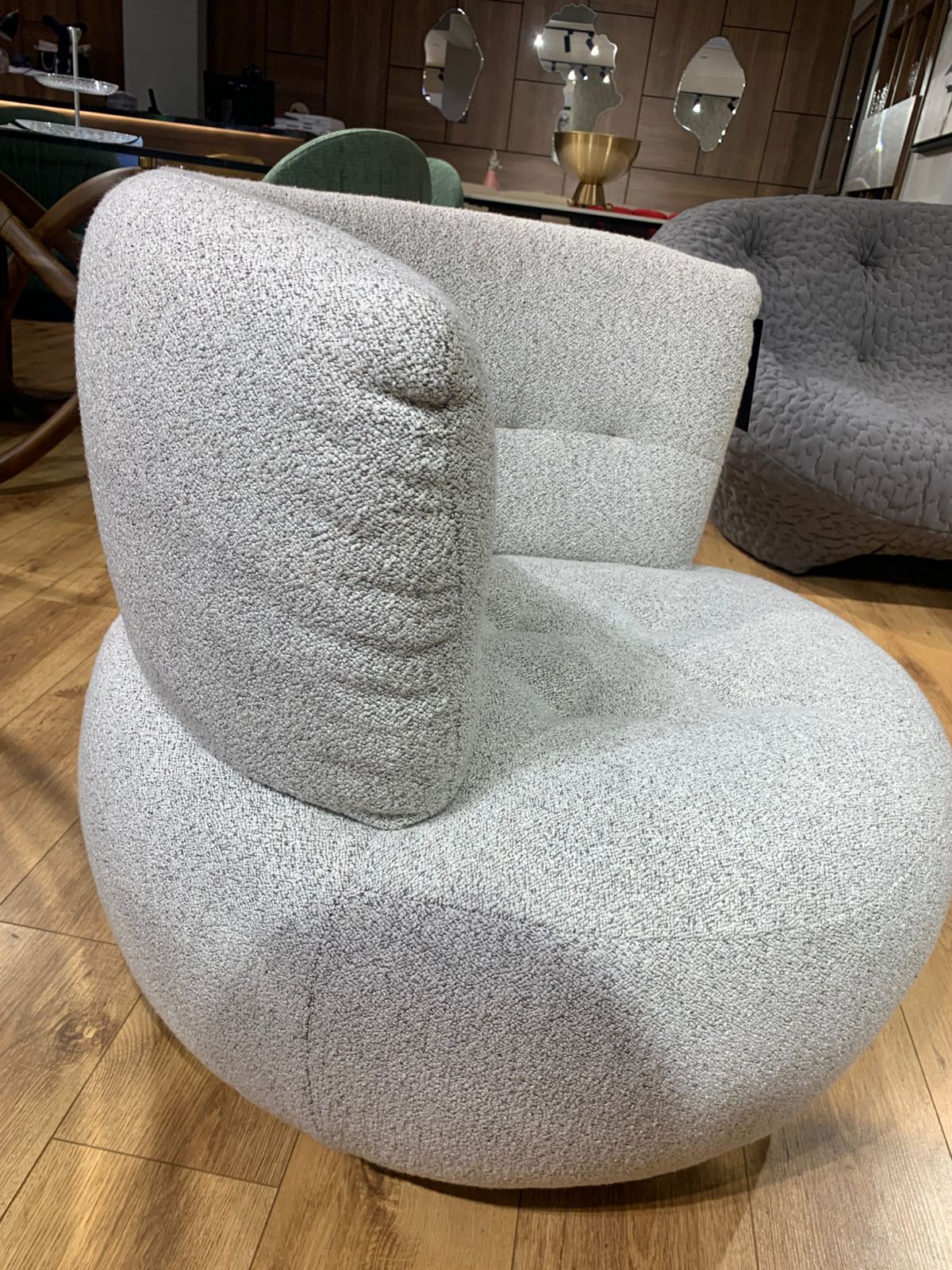 Fauteuil bergère arrondi gris clair en tissu bouclette, dossier enveloppant et assise profonde, style contemporain pour coin détente .