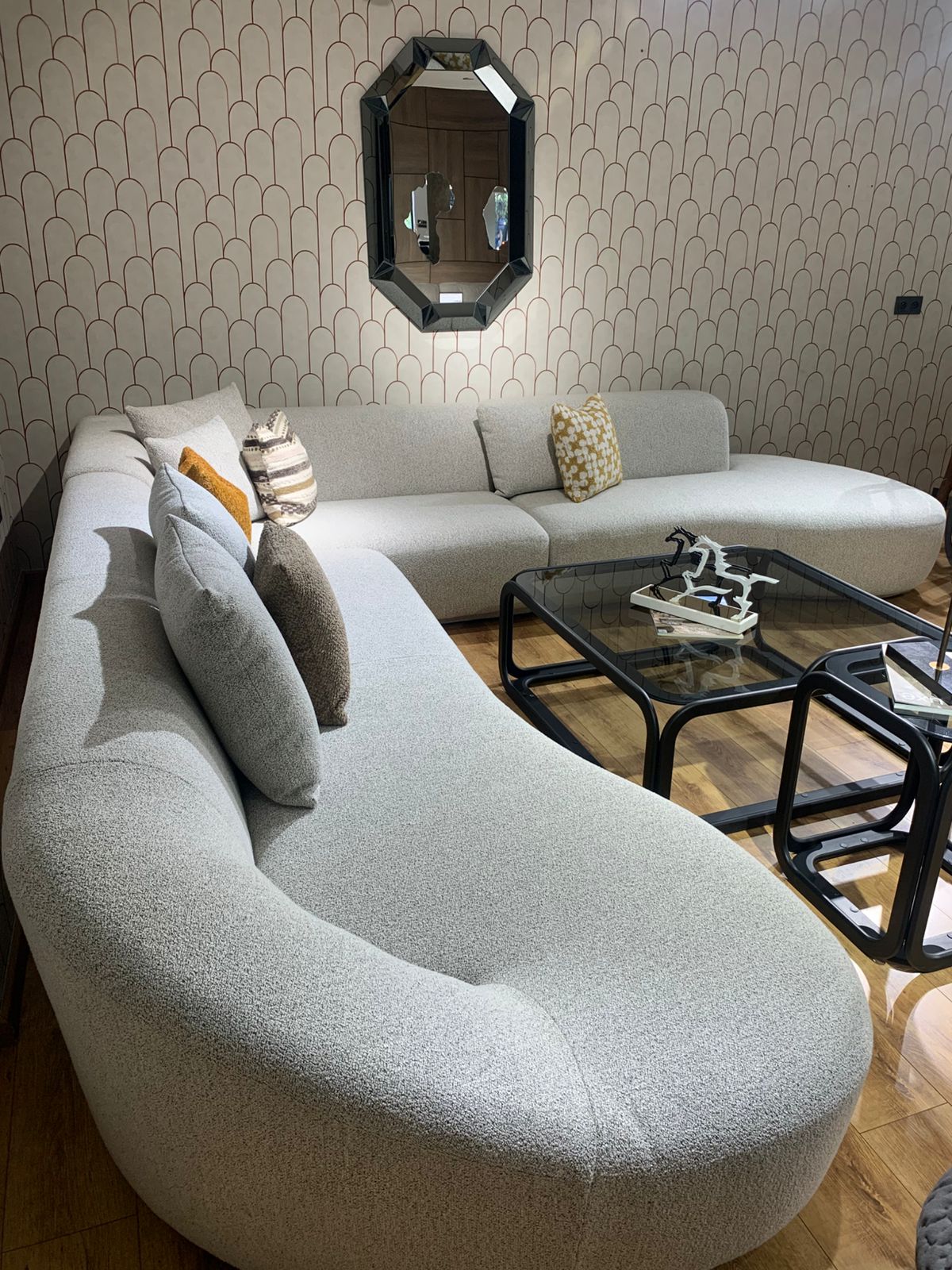 Grand canapé d’angle aux lignes arrondies en tissu bouclé , décoré de plusieurs coussins colorés. 