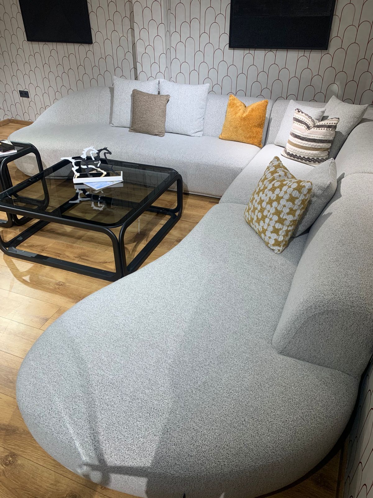 Grand canapé d’angle aux lignes arrondies en tissu bouclé , décoré de plusieurs coussins colorés. 