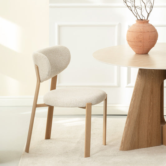 Chaise moderne au design minimaliste avec assise et dossier rembourrés en tissu beige clair, pieds en bois clair naturel, idéale pour salle à manger ou bureau contemporain.
