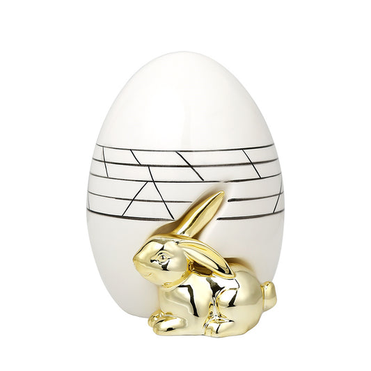Décoration moderne avec lapin doré brillant devant un vase ovoïde blanc aux lignes noires élégantes.