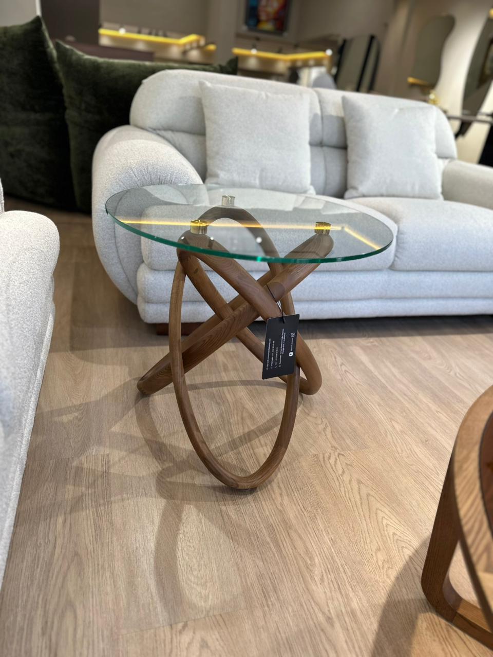 Table d’appoint ronde en verre et bois sculpté, au design moderne avec touches dorées. Élégante, légère et idéale pour un salon contemporain.