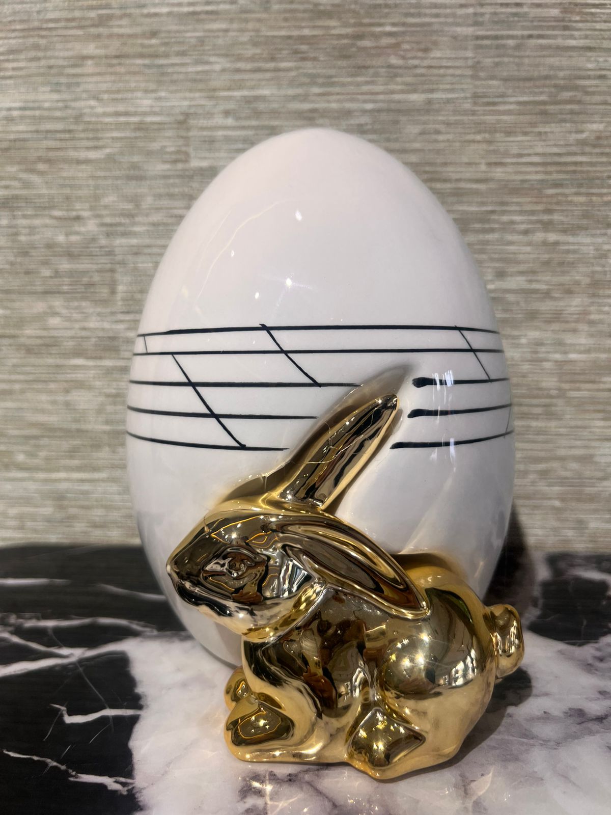 Décoration moderne avec lapin doré brillant devant un vase ovoïde blanc aux lignes noires élégantes.