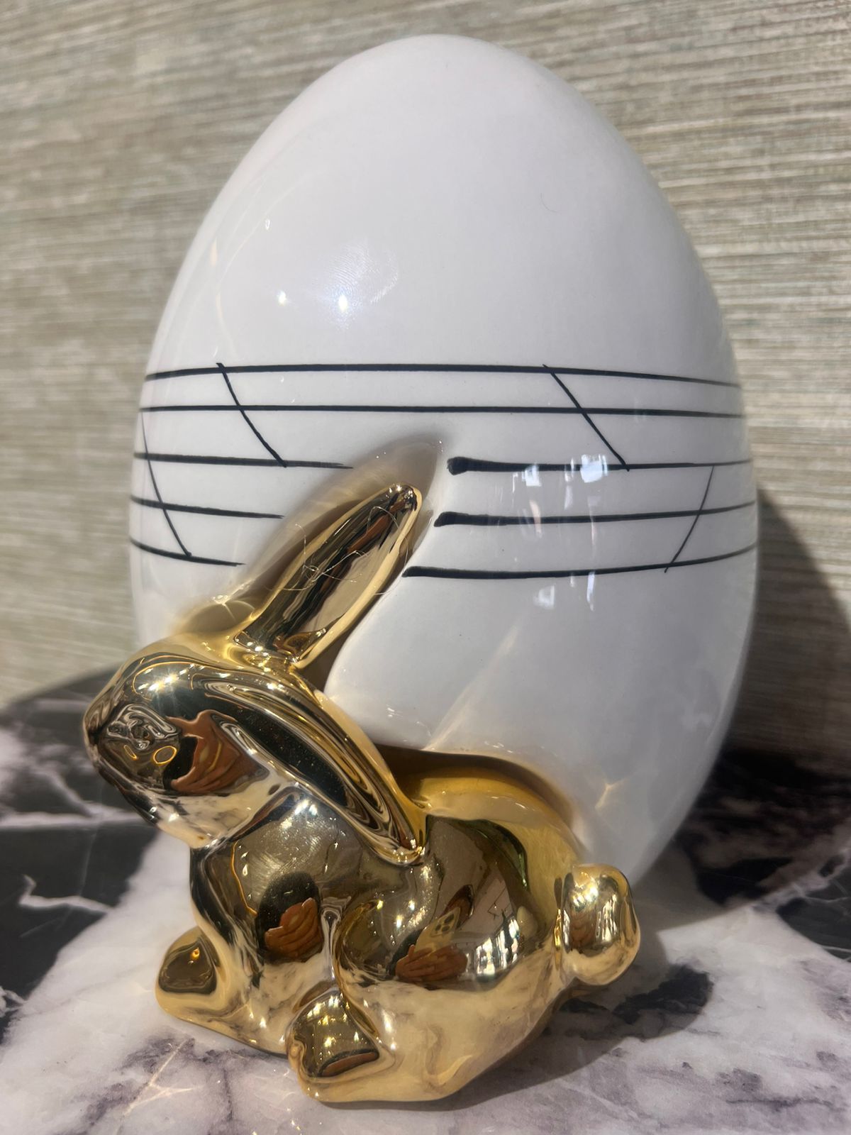 Décoration moderne avec lapin doré brillant devant un vase ovoïde blanc aux lignes noires élégantes.