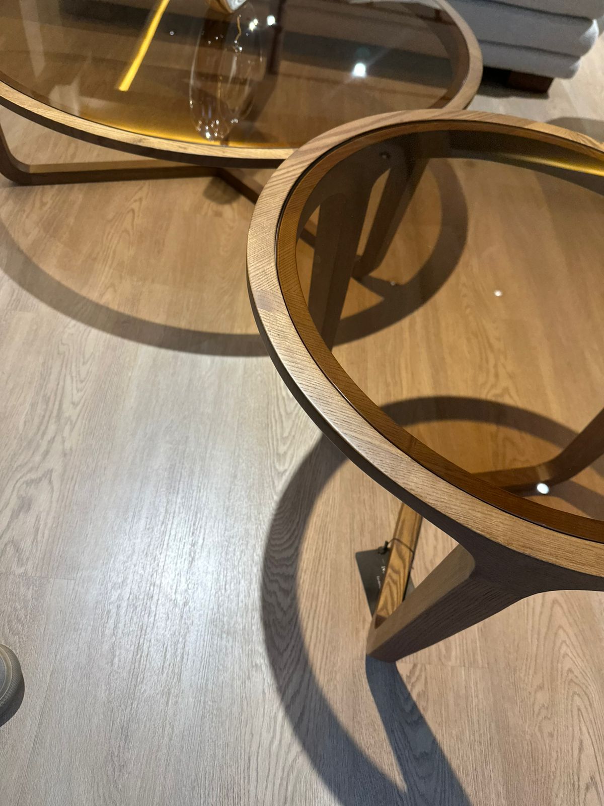 Ensemble rondes en bois de noyer avec plateau en verre teinté ambré, design moderne, placées dans un salon contemporain