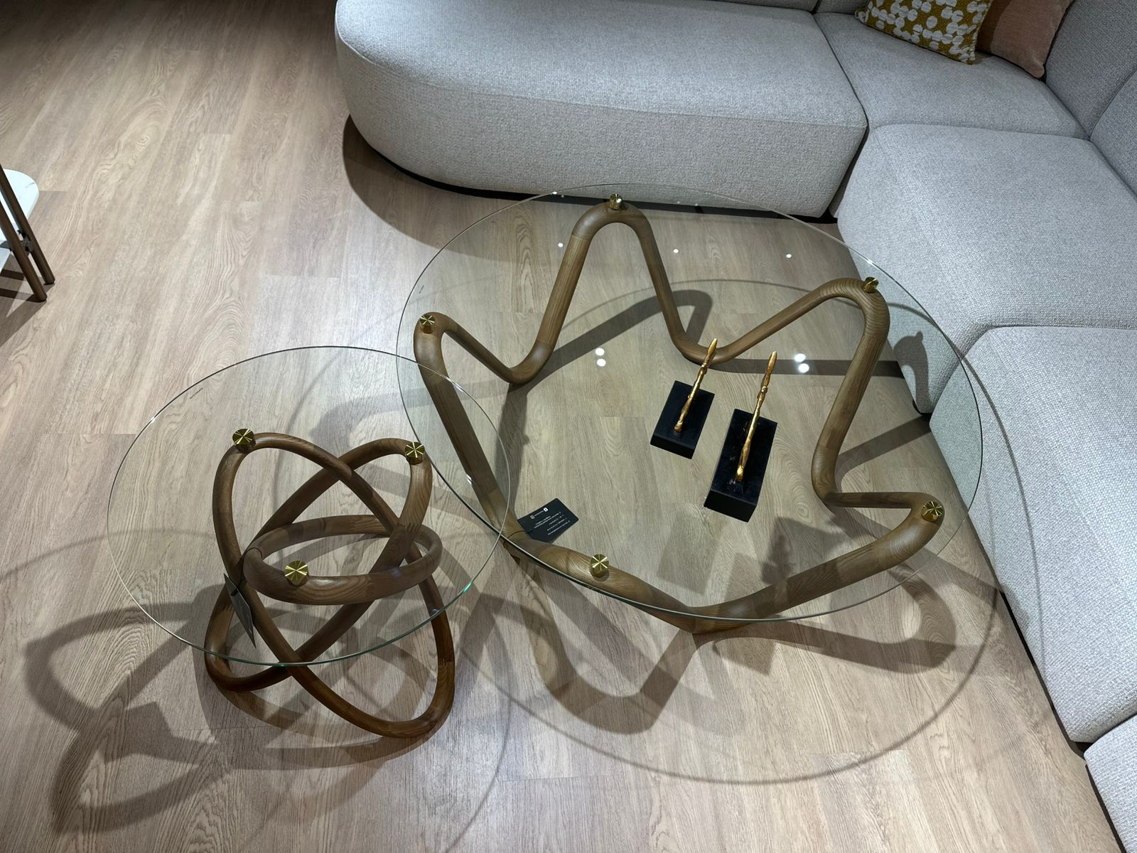 Table basse design avec plateau en verre rond et structure sculpturale en bois courbé, accompagnée d’une table d’appoint assortie.