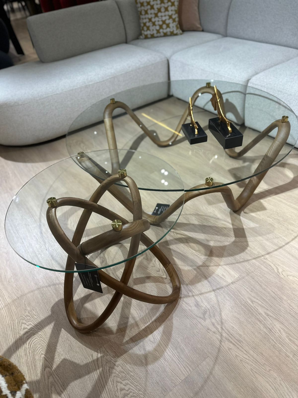 Table basse design avec plateau en verre rond et structure sculpturale en bois courbé, accompagnée d’une table d’appoint assortie.