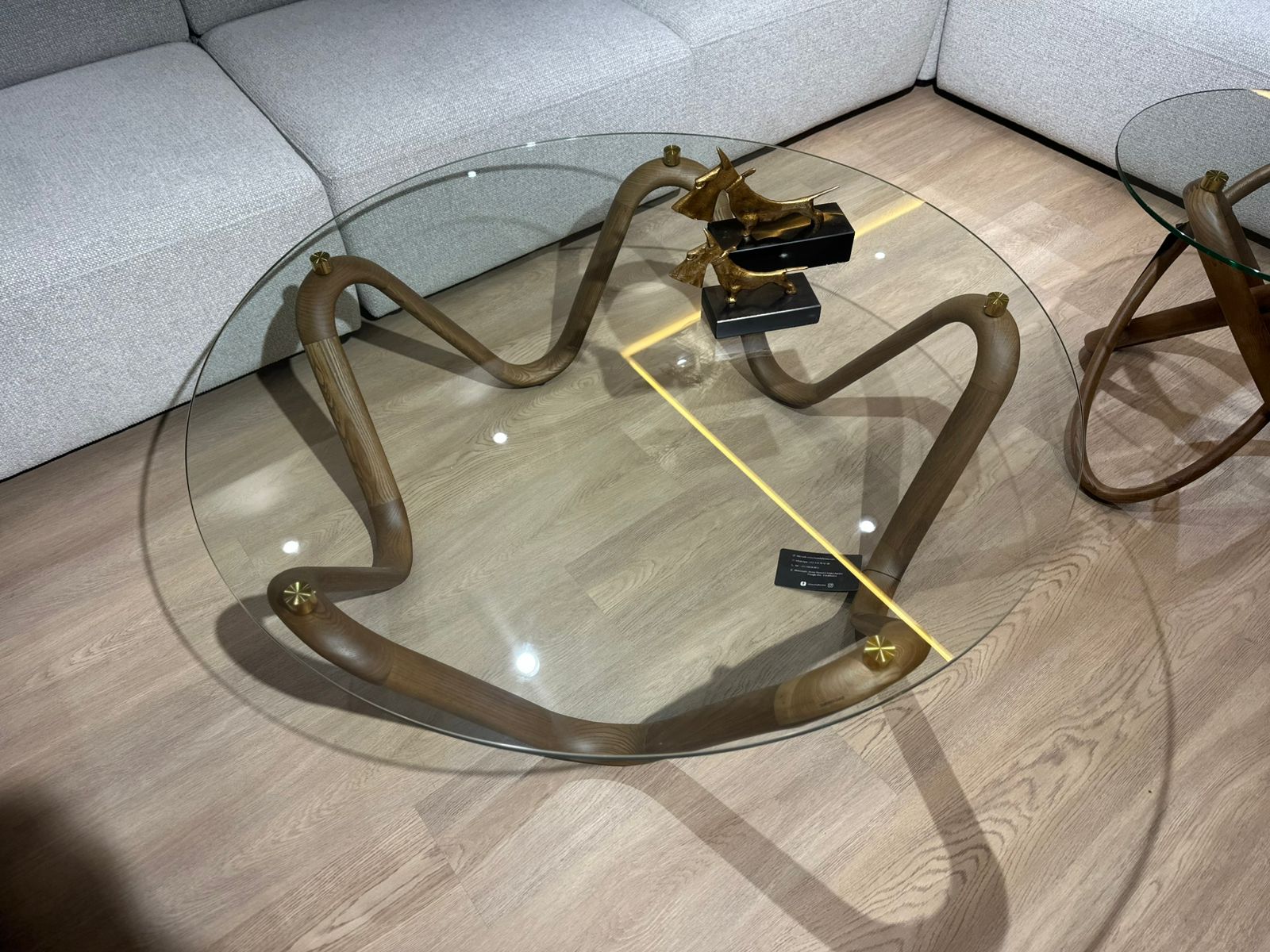 Table basse design avec plateau en verre rond et structure sculpturale en bois courbé, accompagnée d’une table d’appoint assortie.