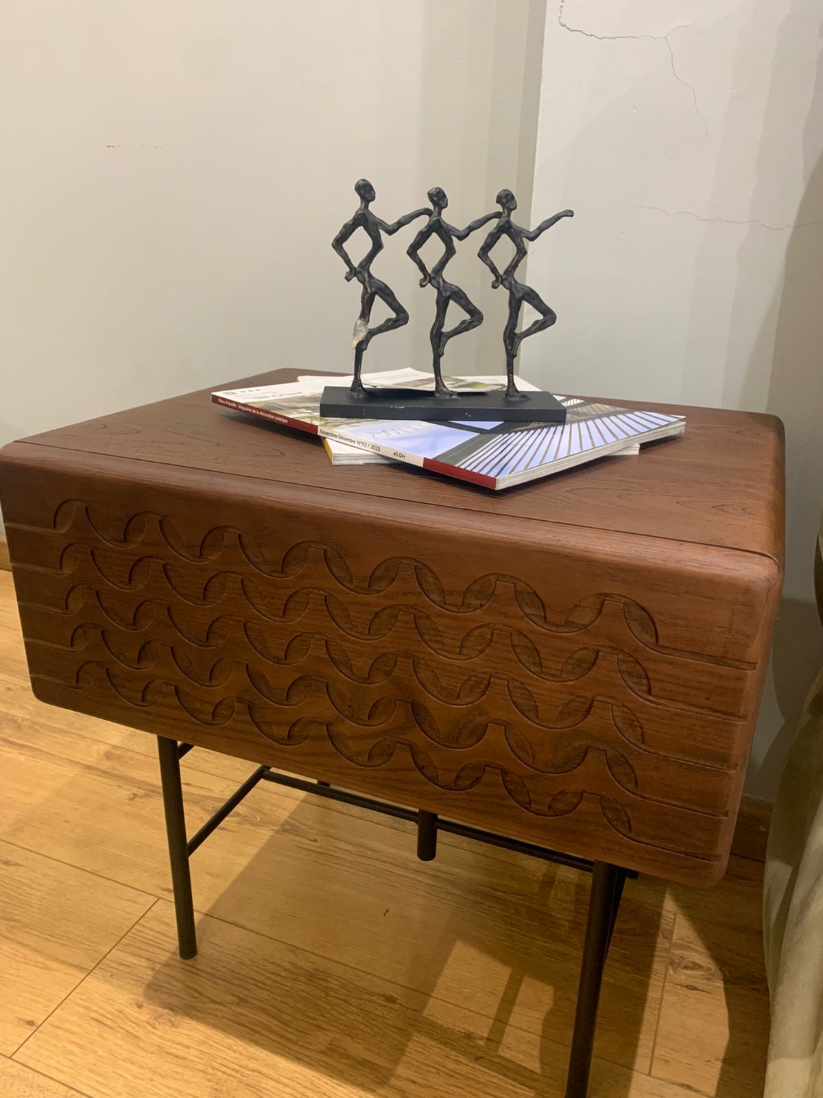 Table de chevet moderne en bois sculpté avec motifs ondulés et pieds en métal noir.