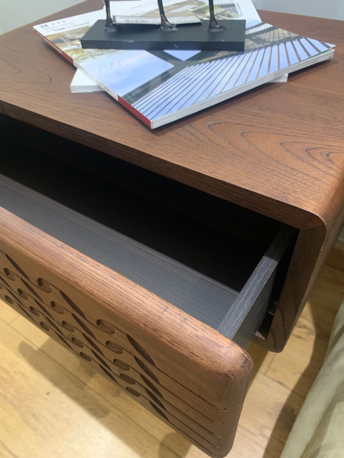 Table de chevet moderne en bois sculpté avec motifs ondulés et pieds en métal noir.