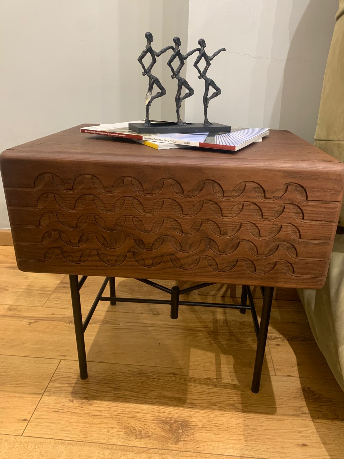 Table de chevet moderne en bois sculpté avec motifs ondulés et pieds en métal noir.