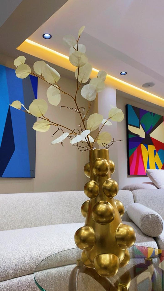 Vase décoratif doré moderne avec reliefs sphériques et branches élégantes sur table de salon contemporain