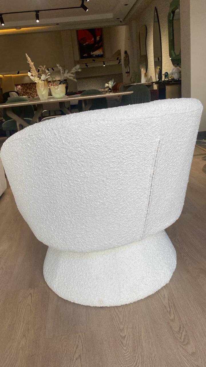 Fauteuil bergère moderne en tissu bouclette blanc avec base pivotante, design arrondi élégant et assise confortable pour salon contemporain.