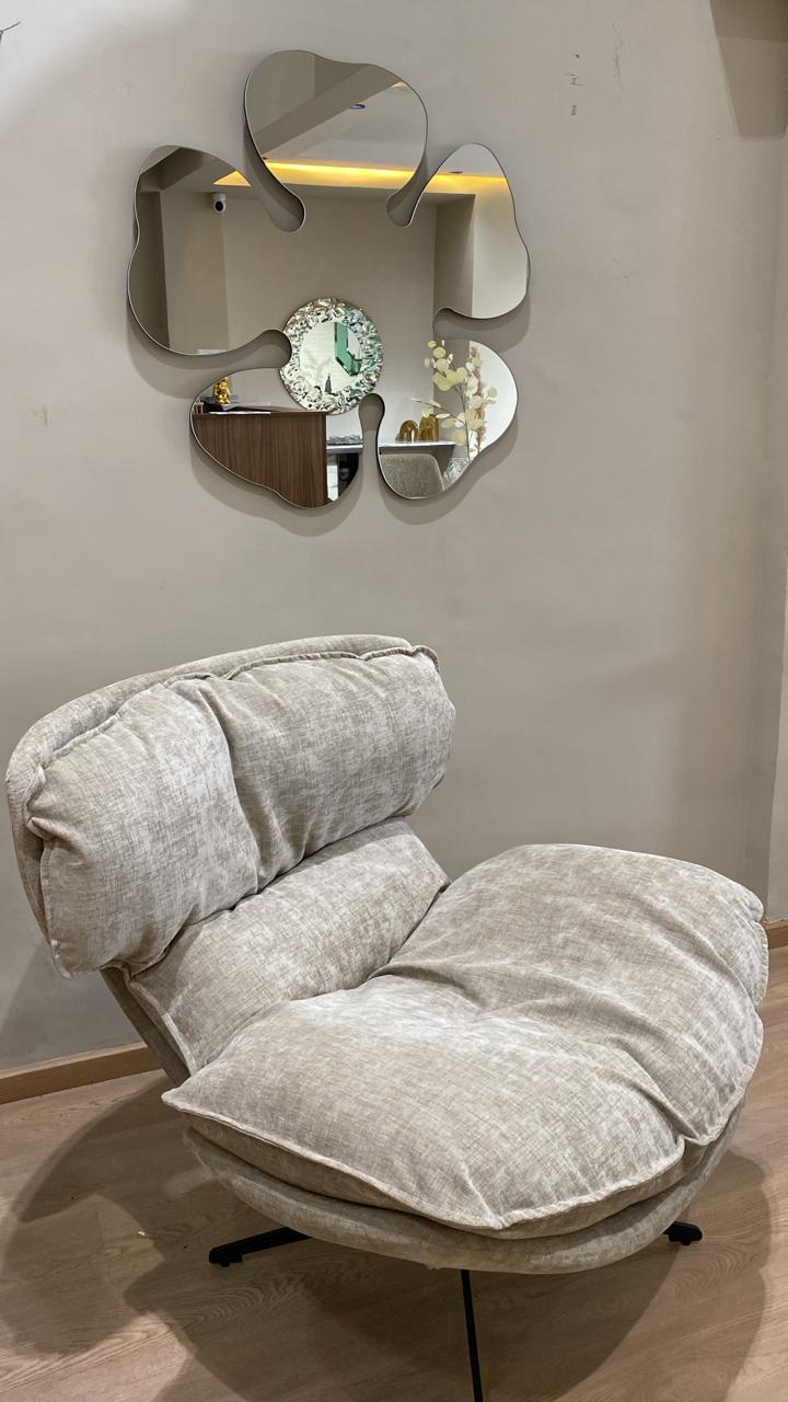 Bergère moderne beige en tissu avec coussins moelleux et pied pivotant noir dans un salon contemporain.