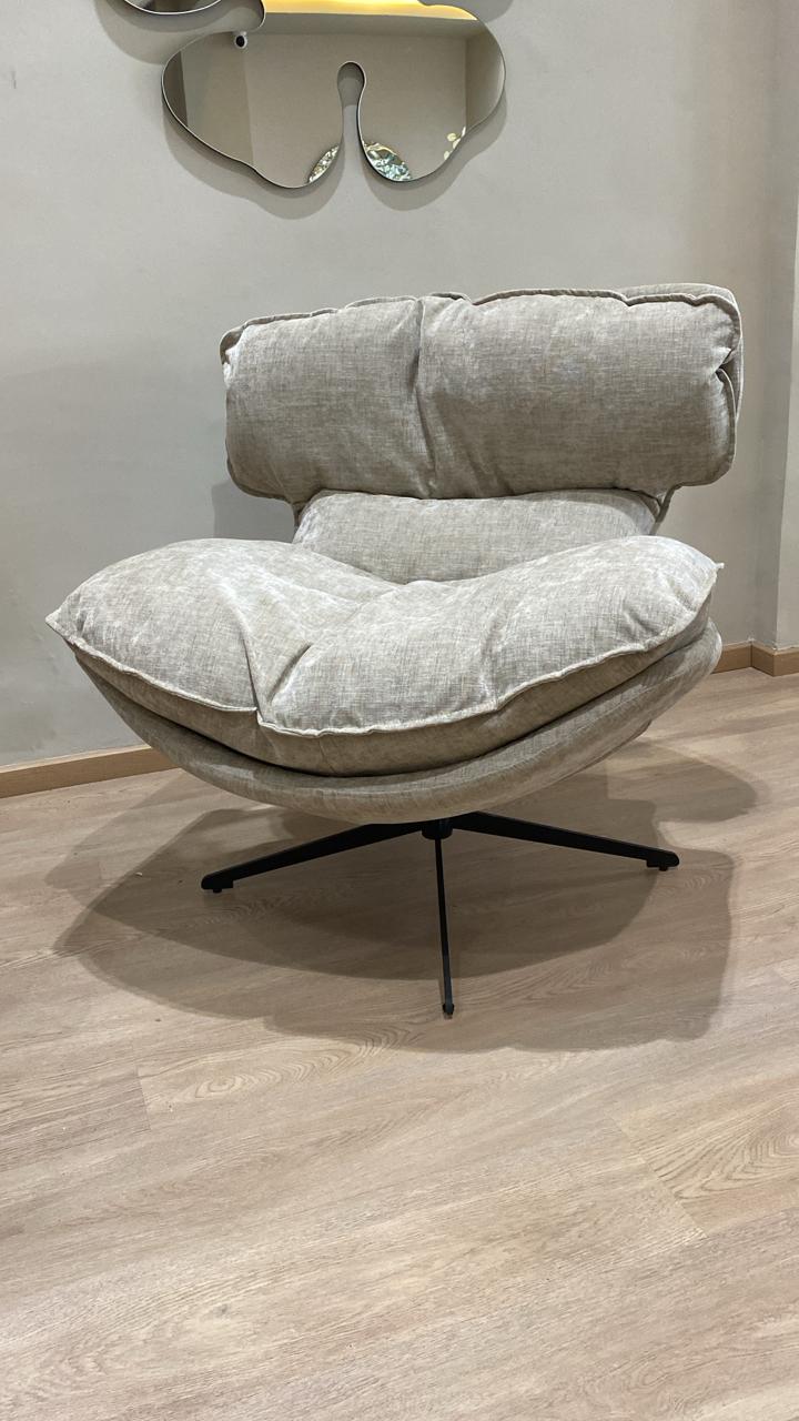 Bergère moderne beige en tissu avec coussins moelleux et pied pivotant noir dans un salon contemporain.