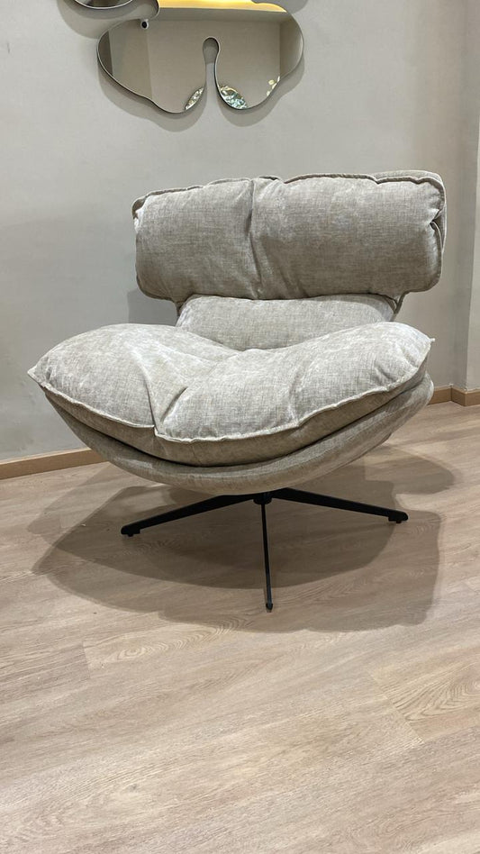 Bergère moderne beige en tissu avec coussins moelleux et pied pivotant noir dans un salon contemporain.