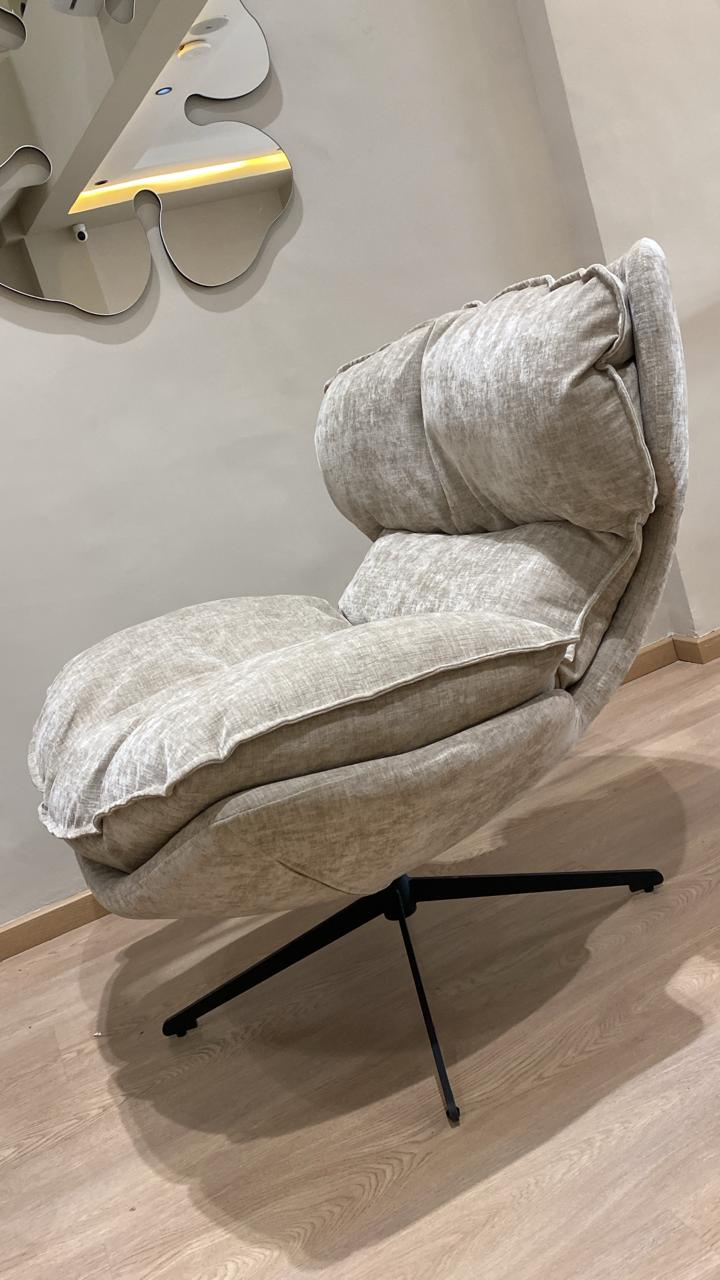 Bergère moderne beige en tissu avec coussins moelleux et pied pivotant noir dans un salon contemporain.