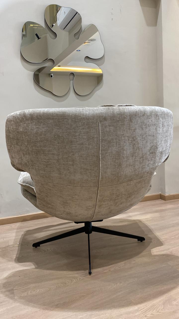 Bergère moderne beige en tissu avec coussins moelleux et pied pivotant noir dans un salon contemporain.