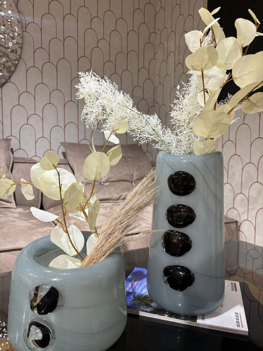 Vase décoratif en céramique bleu gris avec détails noirs en relief, garni de fleurs séchées, posé sur une table moderne dans un intérieur élégant.