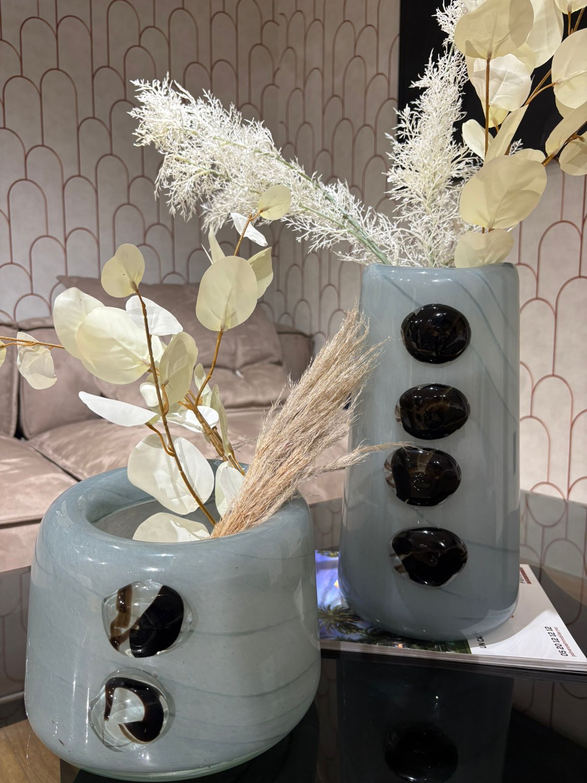 Vase décoratif en céramique bleu gris avec détails noirs en relief, garni de fleurs séchées, posé sur une table moderne dans un intérieur élégant.
