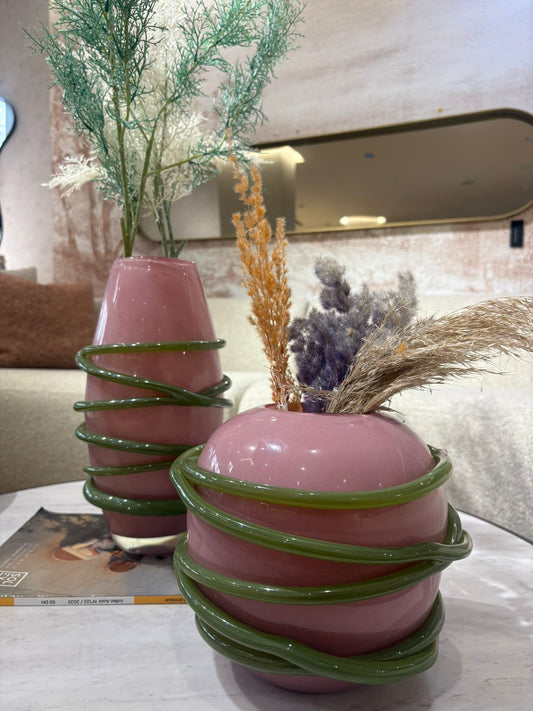 Vase décoratif en verre rose avec détails spiralés verts et fleurs séchées, design moderne et artistique