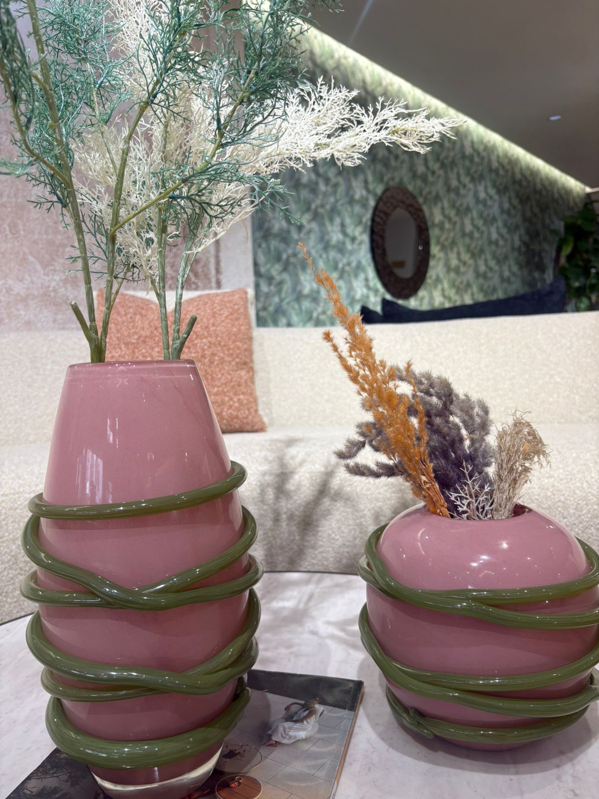 Vase décoratif en verre rose avec détails spiralés verts et fleurs séchées, design moderne et artistique
