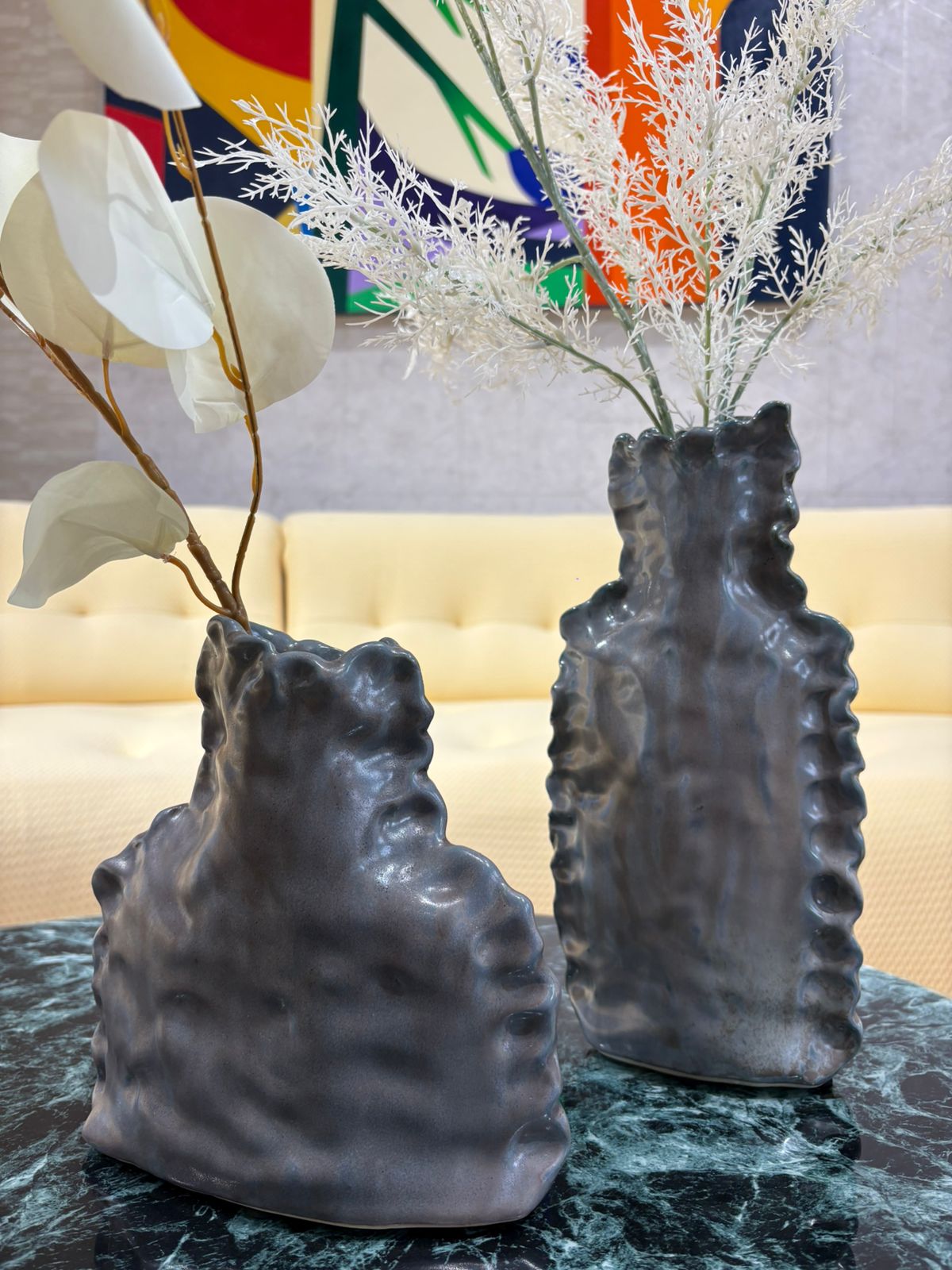 Vase décoratif gris au design sculptural texturé avec fleurs séchées blanches, posé sur une table en marbre dans un intérieur moderne.