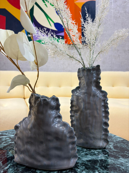 Vase décoratif gris au design sculptural texturé avec fleurs séchées blanches, posé sur une table en marbre dans un intérieur moderne.