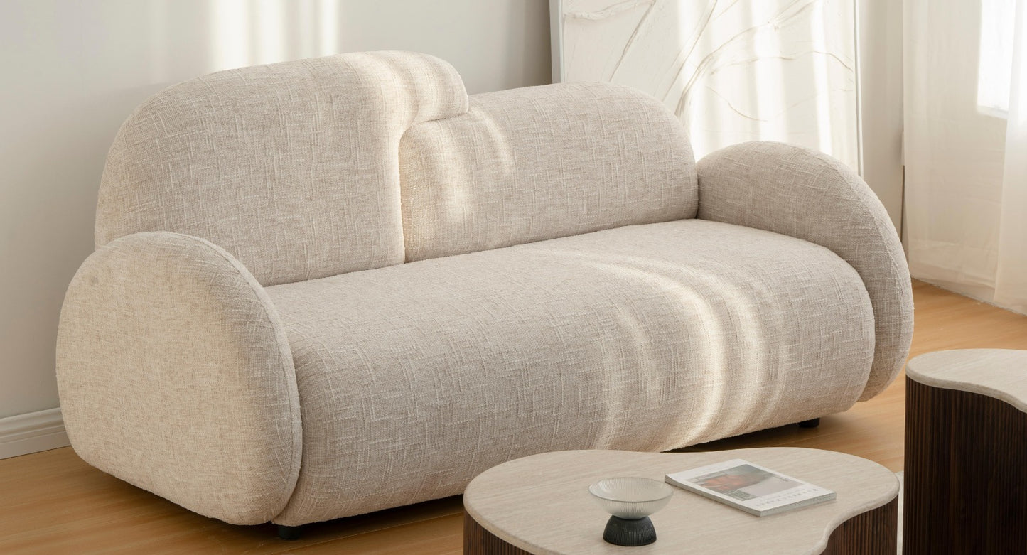 Canapé moderne aux formes arrondies, revêtu d’un tissu texturé, avec accoudoirs larges et assise profonde, installé dans un intérieur lumineux au style épuré.